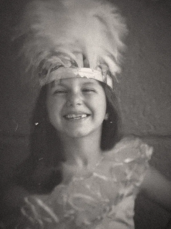 Fotografia antiga de Viviane ainda criança, com um cocar de plumas, sorrindo.