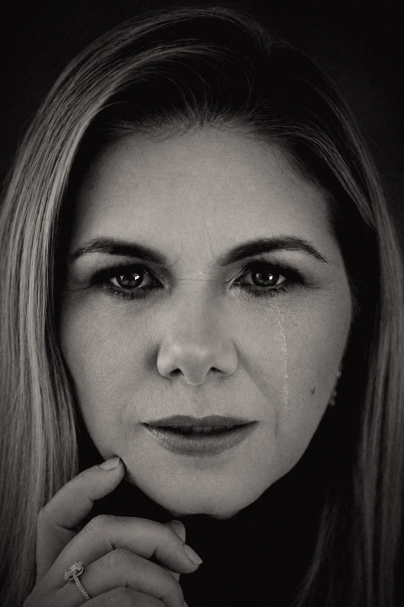 Retrato em preto e branco de Viviane Brunieri, com o olhar sério, uma lágrima no rosto e a mão junto ao queixo.
